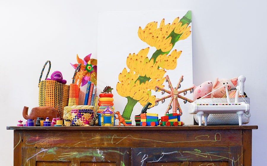 A vintage wooden cabinet with crayon marks on its surface, and on which there is a painting of a banana plant and some toys - Beautiful Homes
