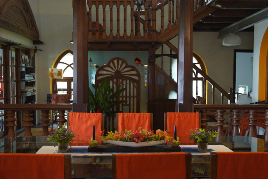 A dining table with six chairs with an orange cloth and behind that is a wooden staircase - Beautiful Homes