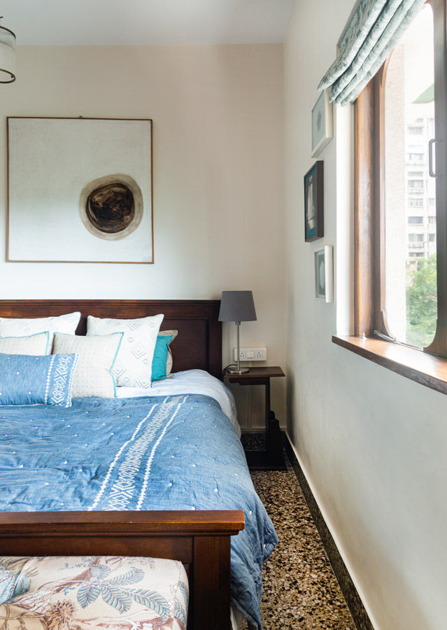 Wooden framed bed with blue and white sheets, abstract art pieces on the wall, natural sunlight from window - Beautiful Homes