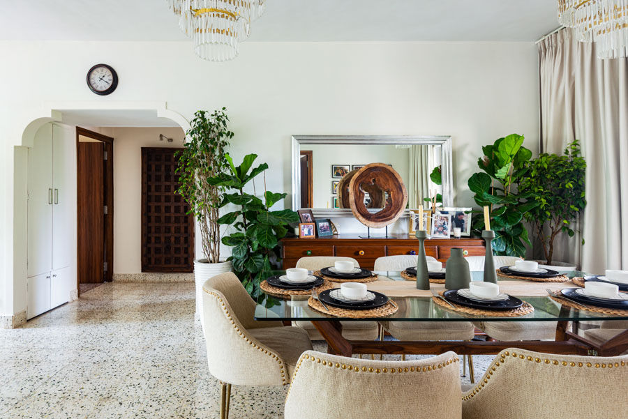 Dining table with a table setting with black plates, jute mats, green candle stands with a wooden cabinet behind it which has frames kept on top of it and a mirror on the wall - Beautiful Homes