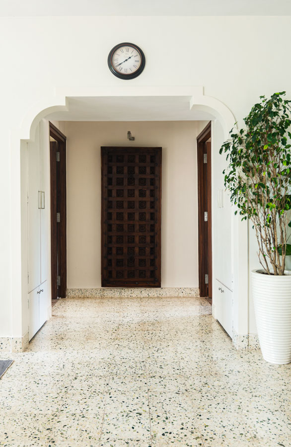 Floor with spotted tiles and wooden doors, white walls with Indian-inspired arch, big indoor plants on the side