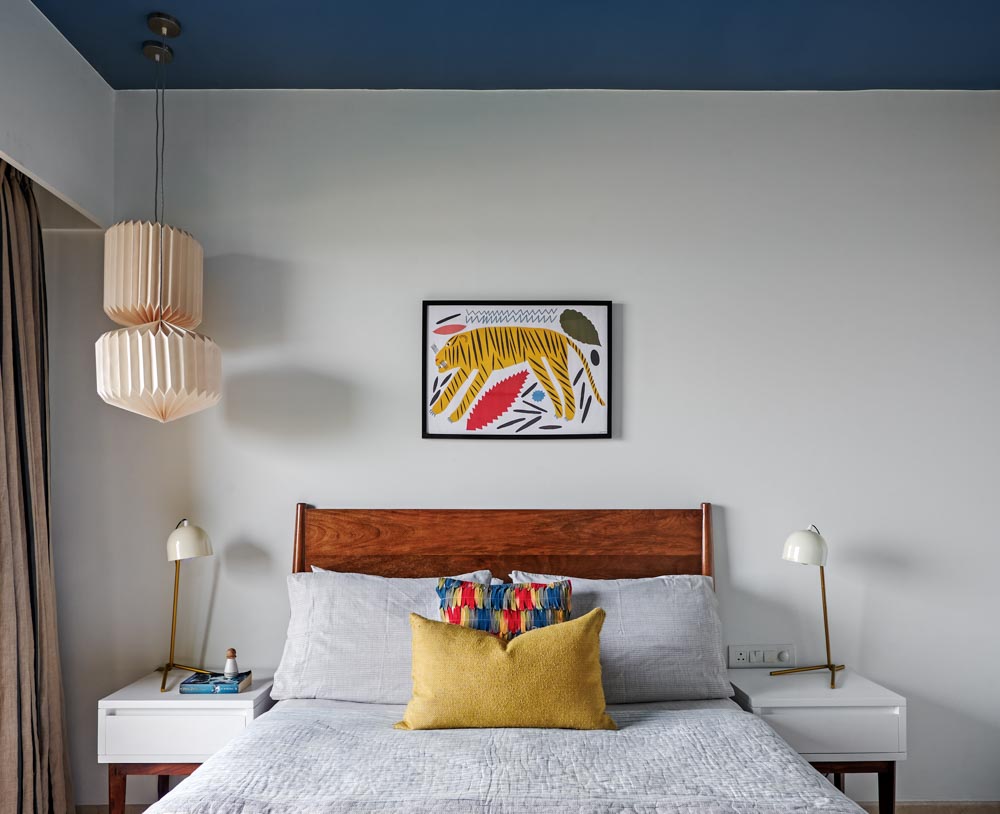 A white bedroom with blue roof, a bed with wooden headboard and an artwork placed on the wall
