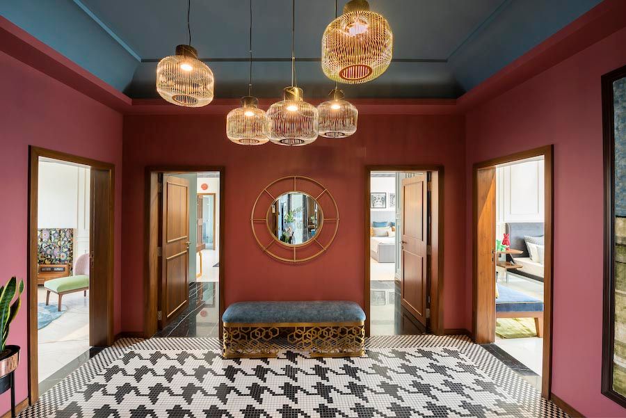 A foyer with access to four rooms with black and white patterned tiles, a bench and a golden framed mirror - Beautiful Homes