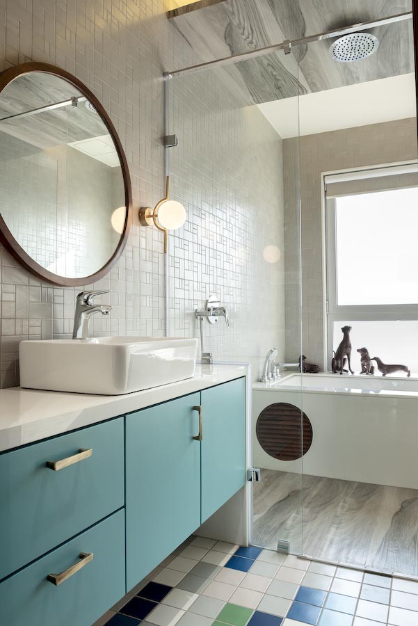A bathroom with different coloured patterned tiles, a bathtub and a sea green cabinet