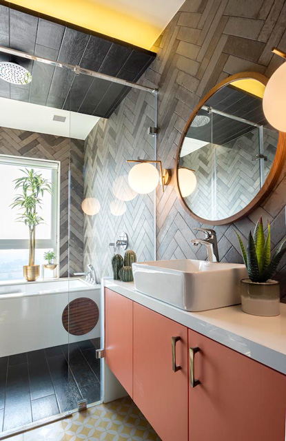 A bathroom with a pale orange cabinet, textured wall tiles, a circular wooden framed mirror and a bathtub