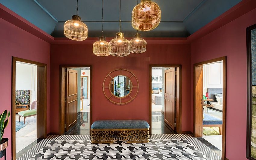 A foyer with access to four rooms with black and white patterned tiles, a bench and a golden framed mirror