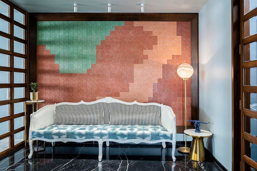 A foyer with a large sofa with blue fabric, patterned tiles on the wall behind it, a side table and a standing lamp next to it - Beautiful Homes