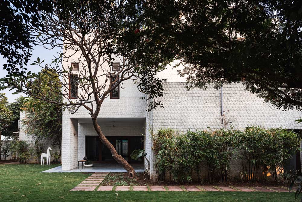 A two storied white brick structured house of designer Leela Shiveshwarkar with greenery surrounding the house - Beautiful Homes