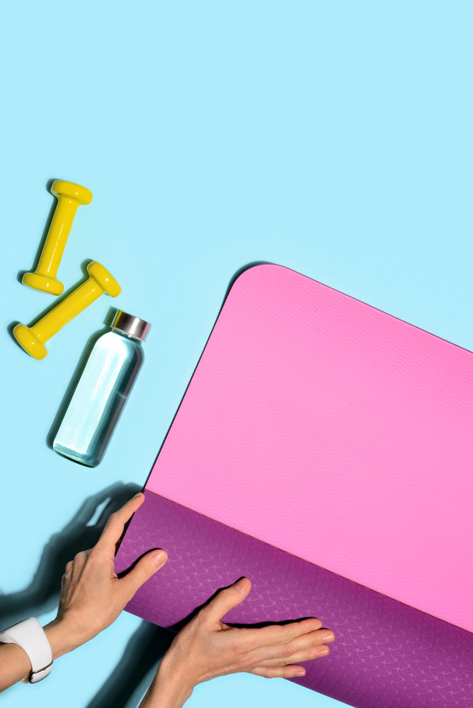 A pair of hands folding a pink yoga mat