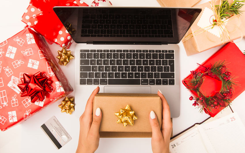 A pair of hands holding a gift box in front of a laptop screen