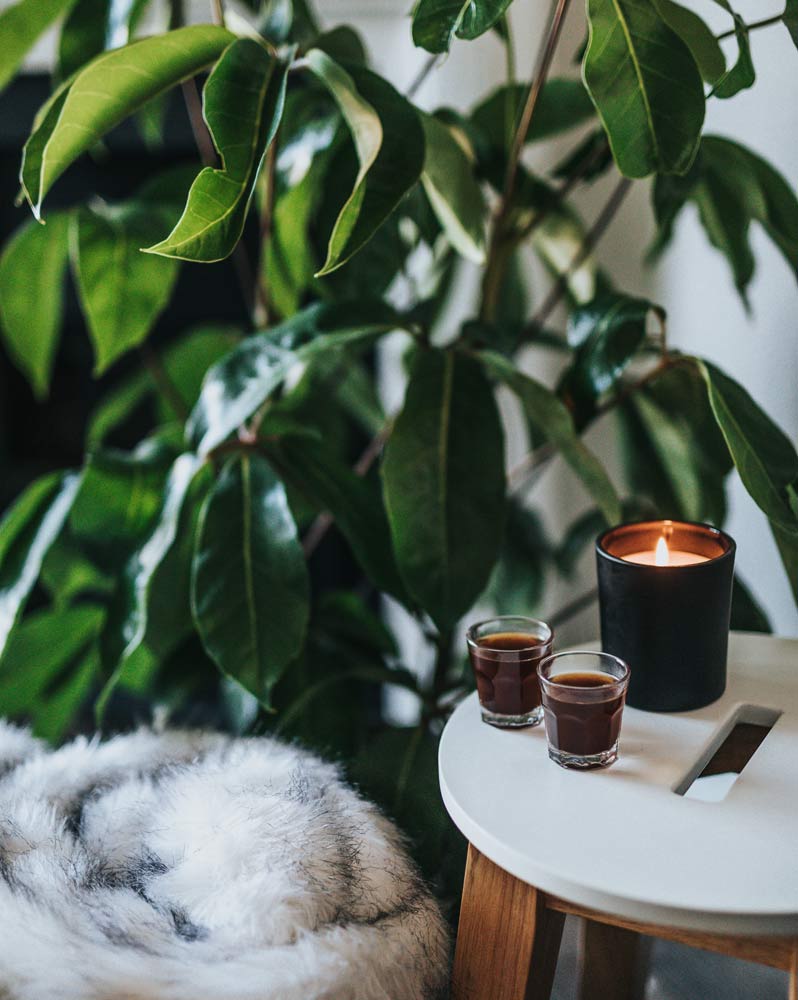 A scented candle placed on a stool with a plant beside it