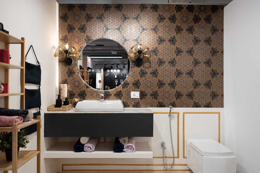 A tiled bathroom with a round mirror, two lamps on each side and soap dispensers besides the basin