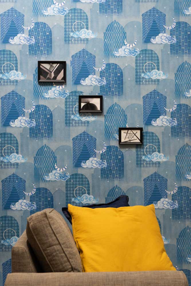 A blue wallpaper covering a wall with small frames hung on it