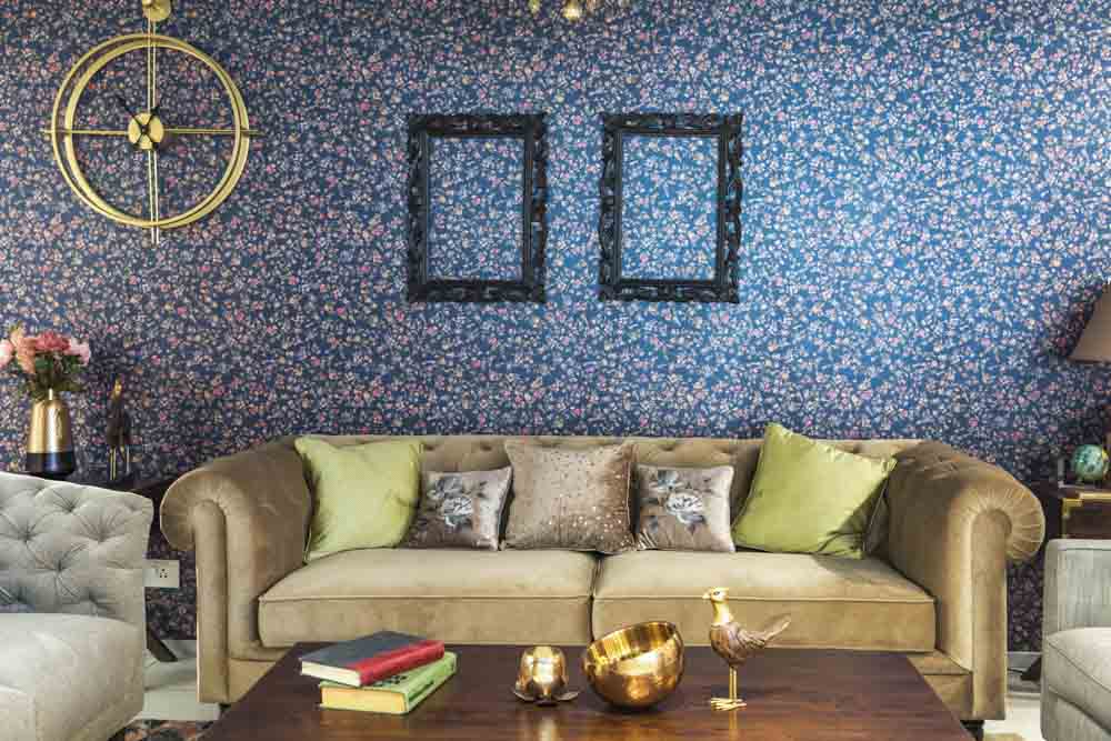 A living room with a purple floral wallpaper, a grey sofa and a wooden coffee table