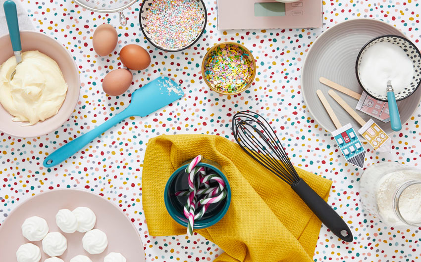 A table top with baking accessories like a spatula, a whisker, flour and a yellow cloth