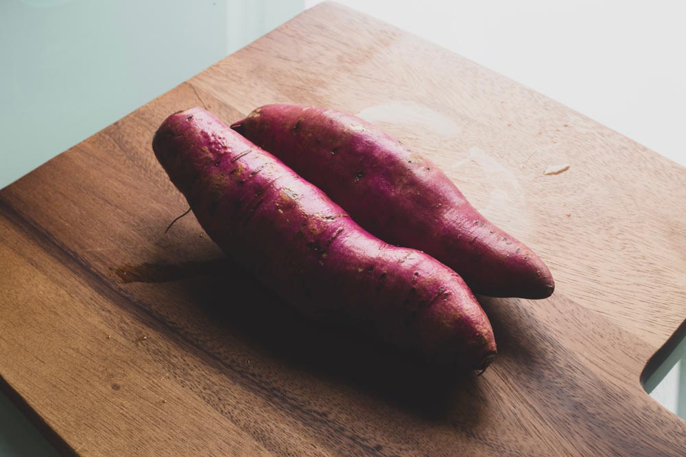 Two sweet potatoes placed on a wooden chopping board