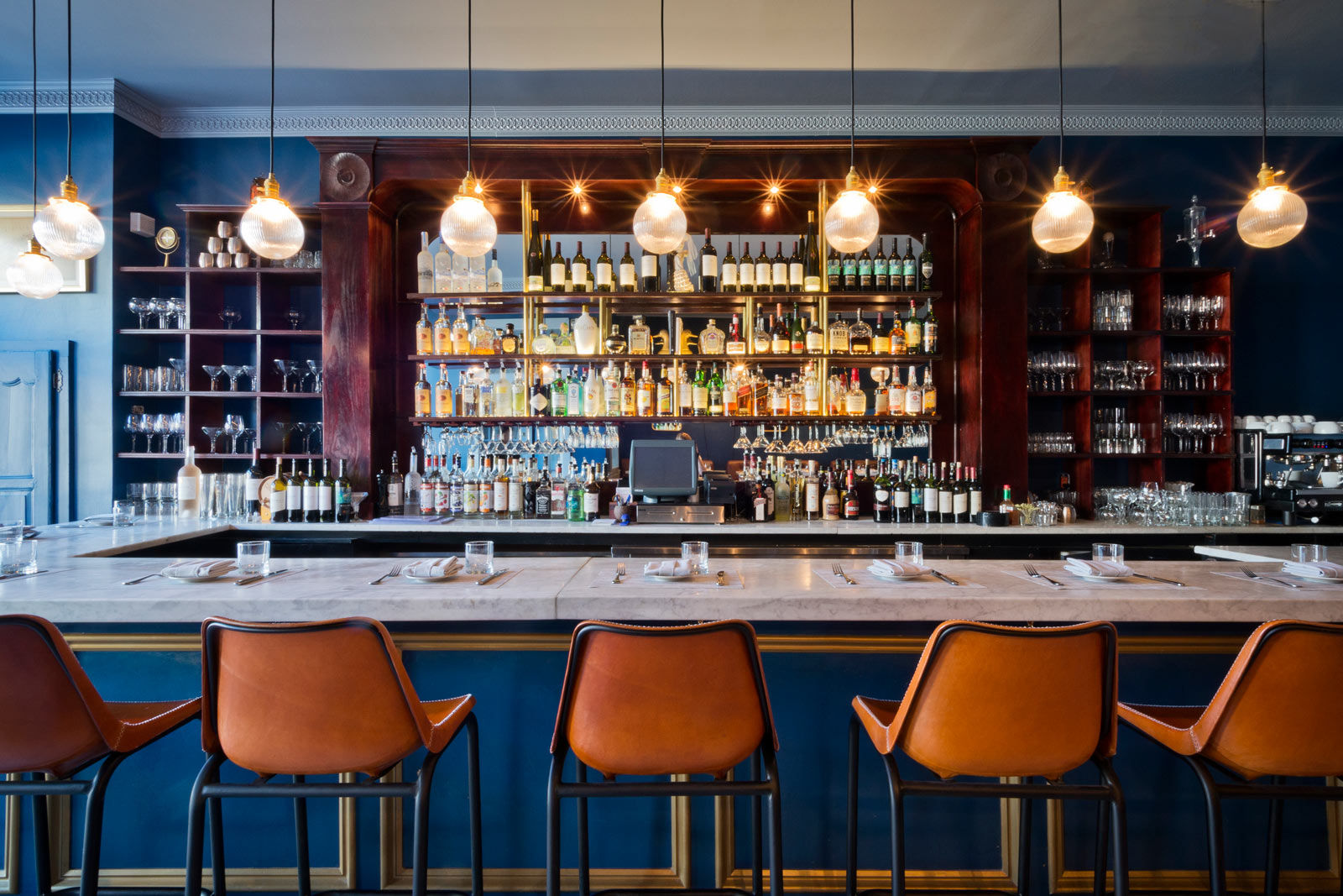 Simple, round pendant lights are suspended over the marble top bar counter - Beautiful Homes