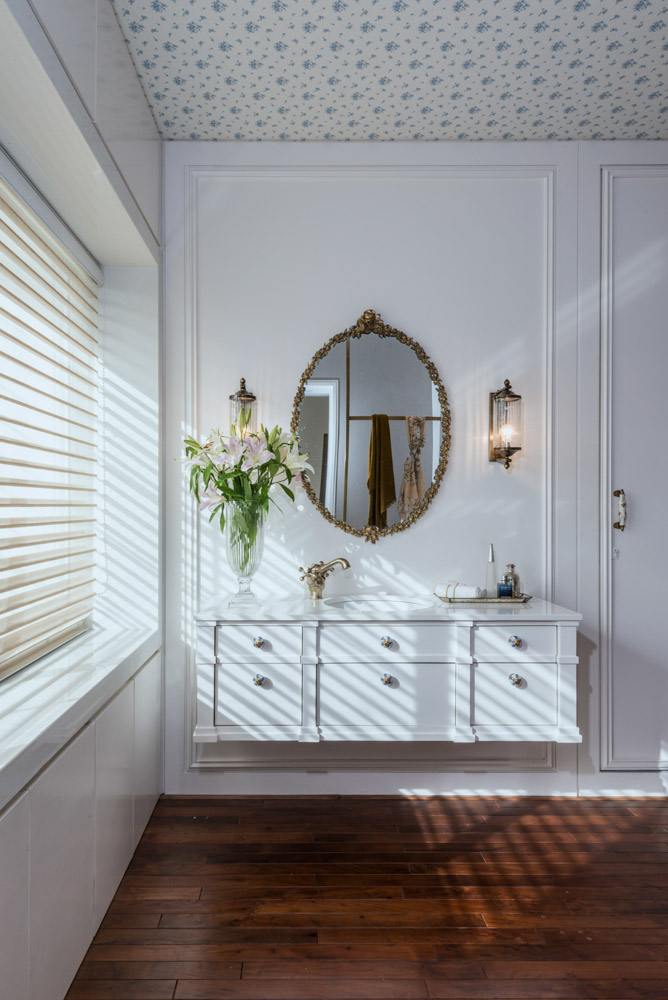 White vintage inspired bathroom with patterned wallpaper on the ceiling, mirror and flower vase