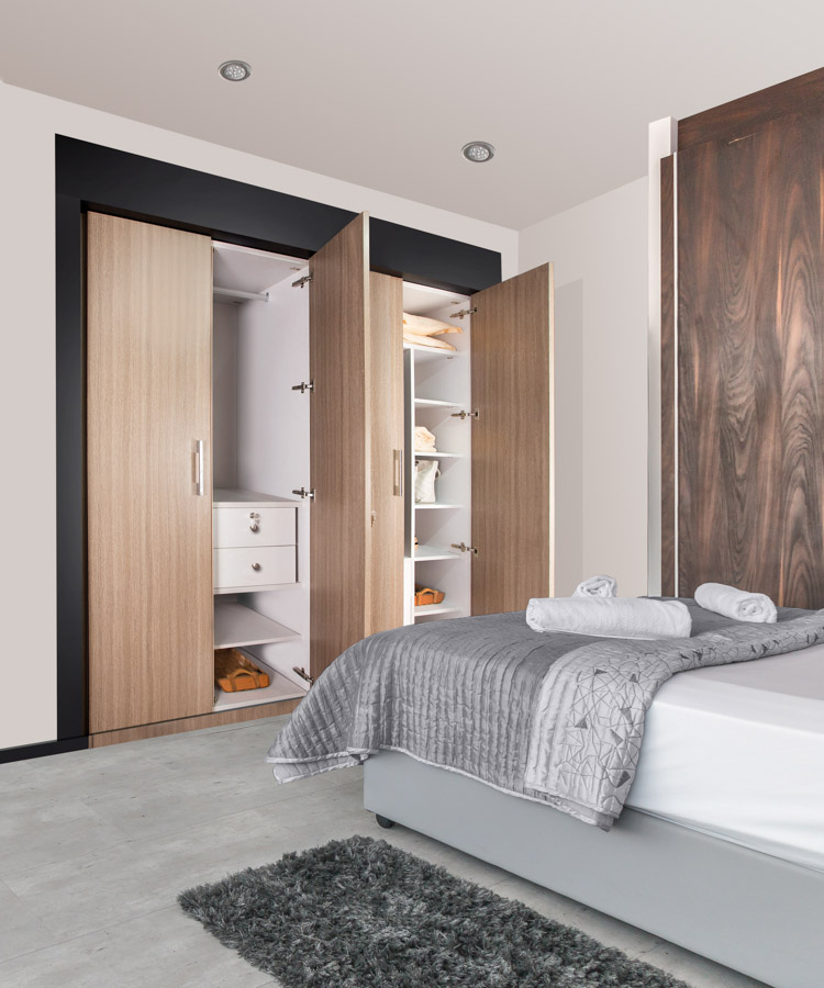 A bedroom with an open wardrobe that has clothes and other items inside