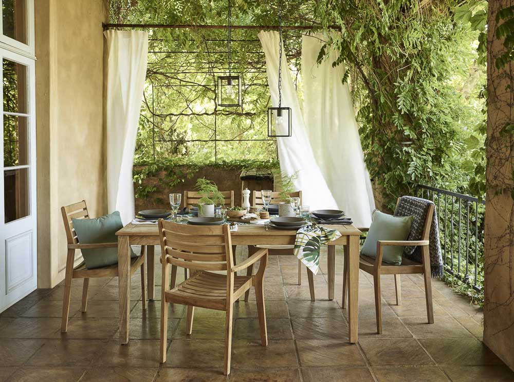 Teak wood dining table set in outdoor green setting - Beautiful Homes