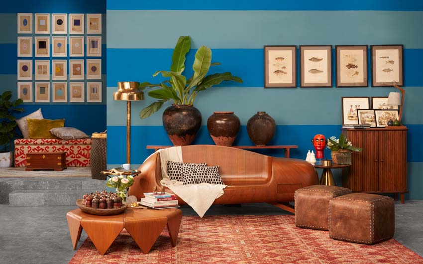 A living room with striped blue walls, a wooden sofa, a large red rug and frames on the wall