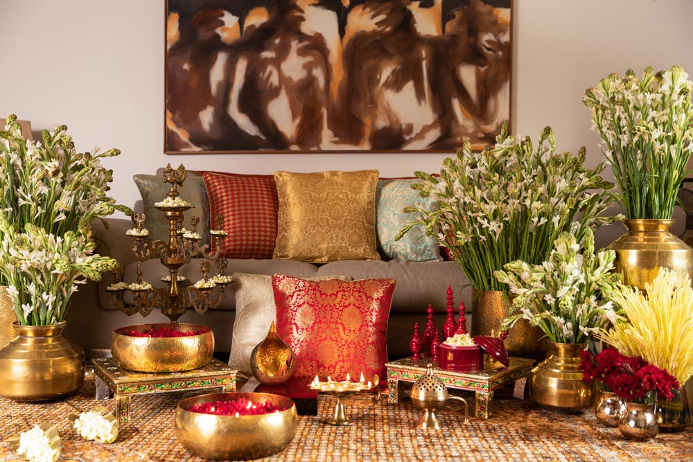 A living room styled for Diwali with a brown sofa, brass diya stands and brass vases