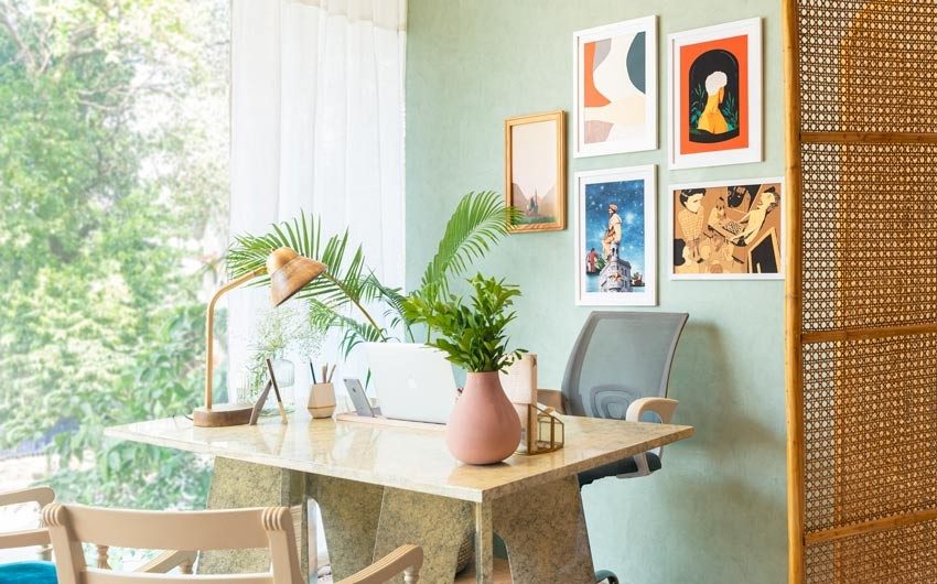 A study table with a laptop placed on it, a rattan room divider and some frames hung on the wall