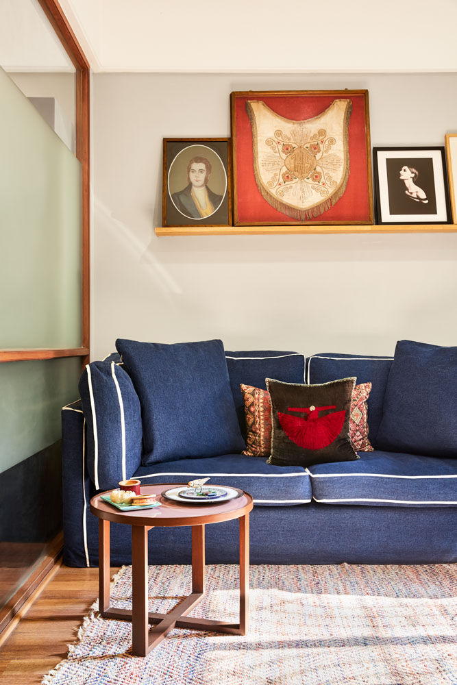 Room with a blue sofa, a rug, a coffee table and frames resting on a wooden platform on the wall behind the sofa - Beautiful Homes