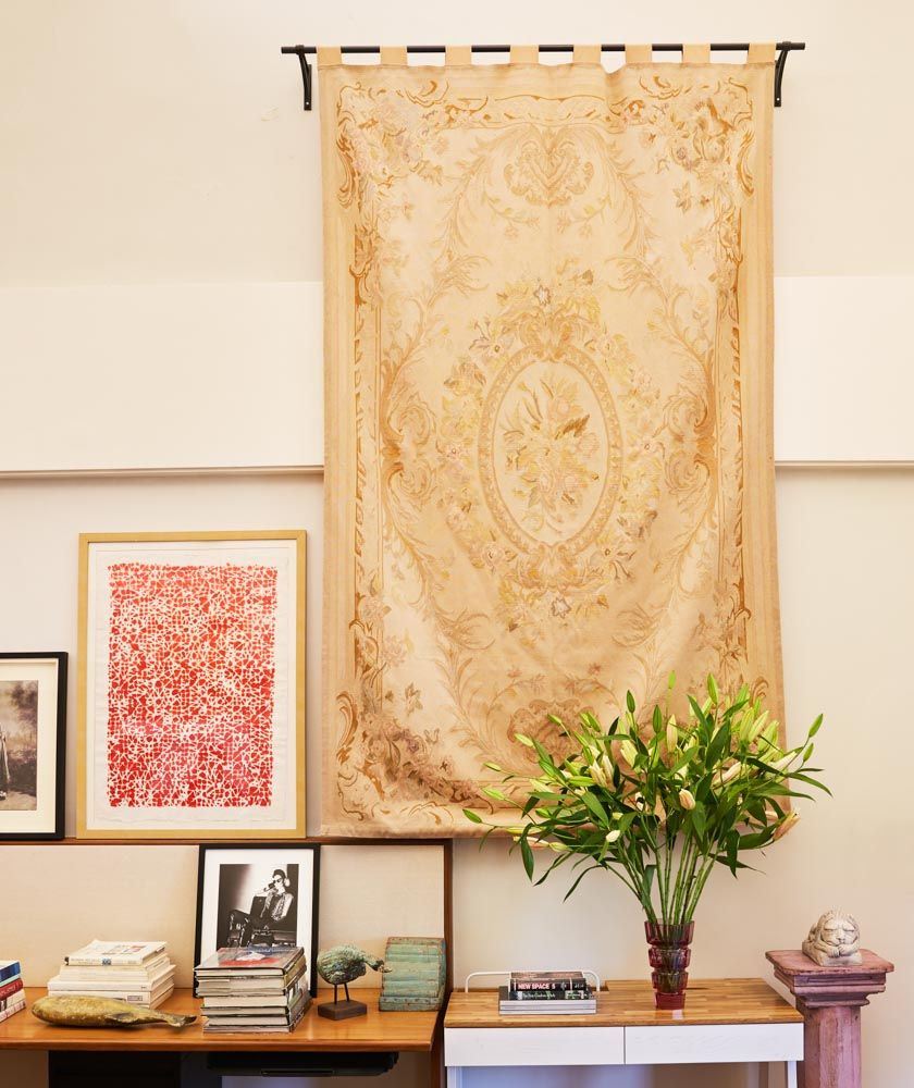 A rug hung from a black rod on a wall, a red artwork next to it and a flower vase on a table beside the wall - Beautiful Homes