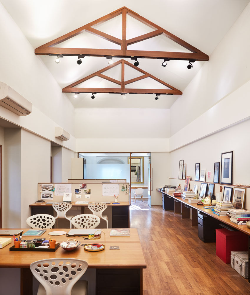 An office space with a high roof with wooden arches, work desks and a table running along the wall with paintings and books put on it - Beautiful Homes