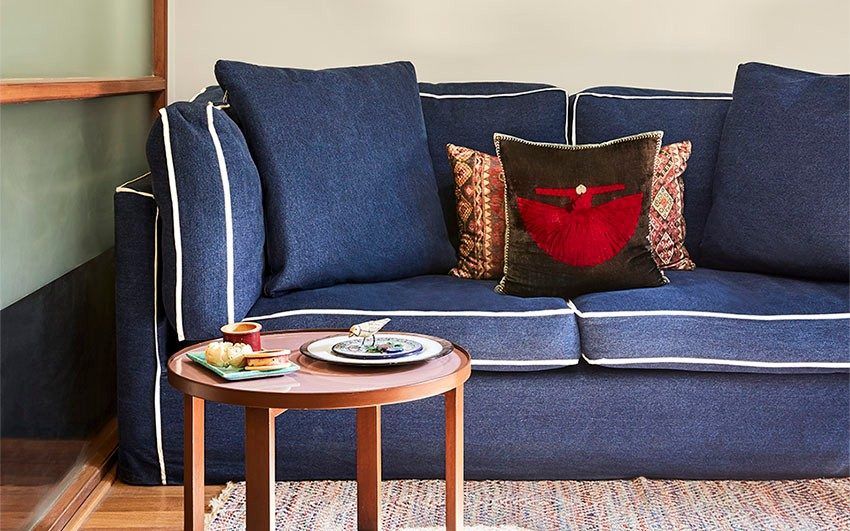 Room with a blue sofa, a rug, a coffee table and frames resting on a wooden platform on the wall behind the sofa - Beautiful Homes