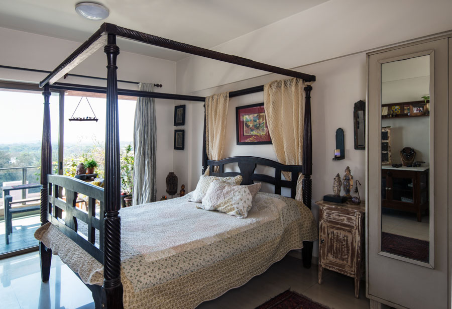 Modest bedroom design with intricate but subtle bedspread and pillows, a wooden candle stand create the perfect Indian bedroom design - Beautiful Homes